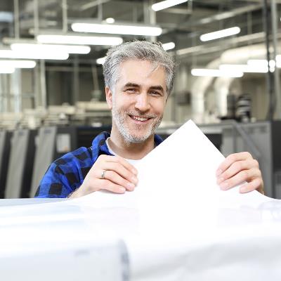 Ein Mann in einer Druckerei der einen Papierbogen prüft.